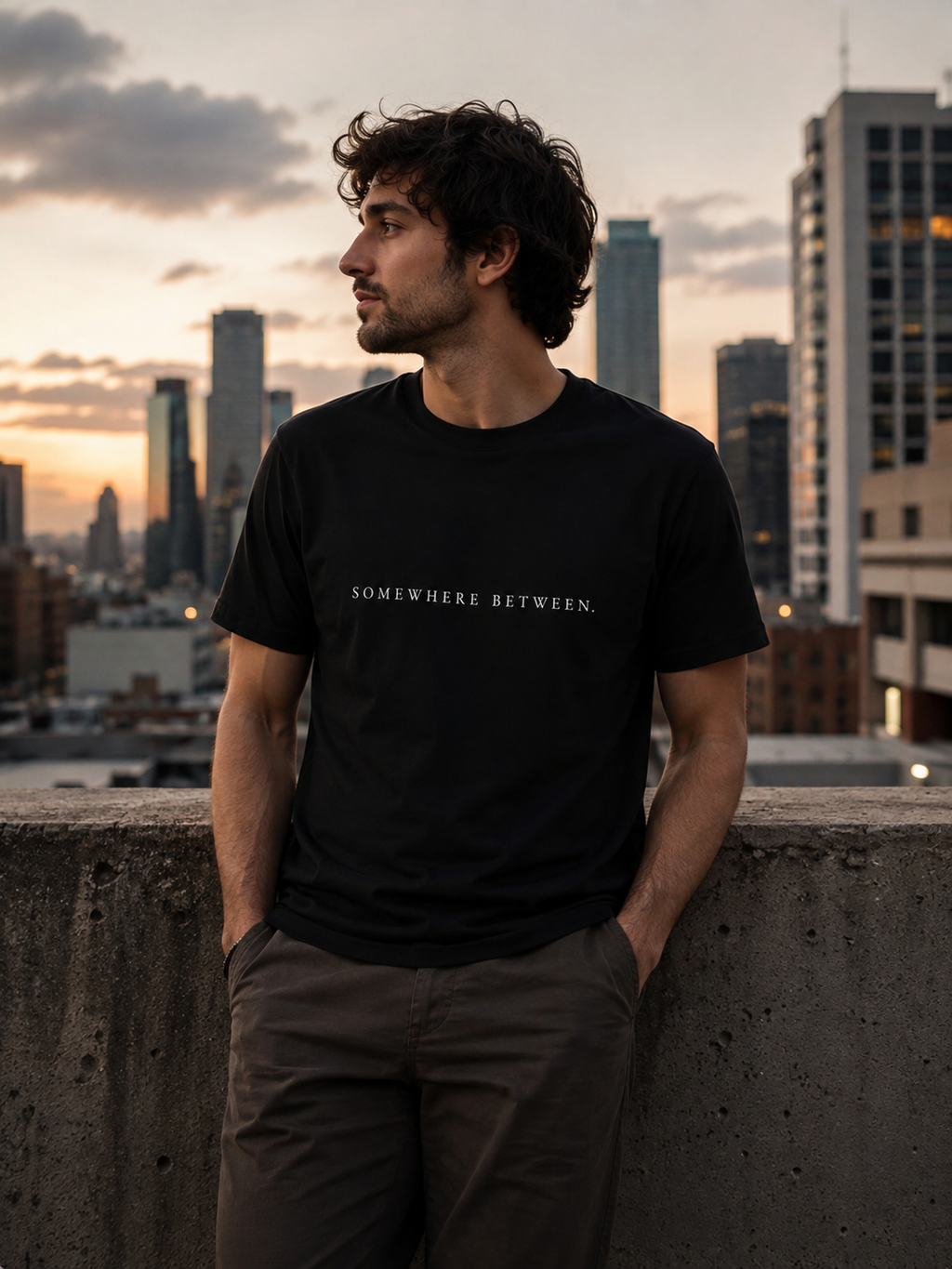 Man wearing black EVAREN Somewhere Between Tee in an urban setting at sunset
