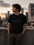 Man wearing black EVAREN Somewhere Between Tee in an urban setting at sunset