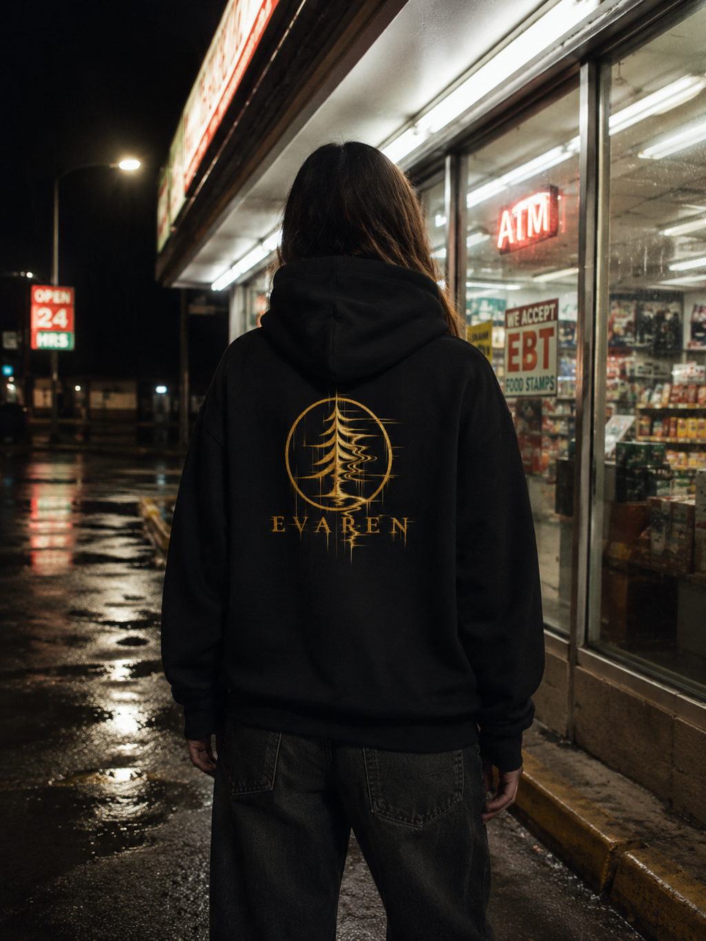Person wearing The Distortion Hoodie by EVAREN outside a convenience store at night, showing the gold distorted evergreen back graphic.