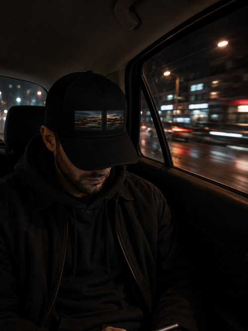 Man wearing The After Passing Cap in the back seat of a car at night with blurred city lights outside.