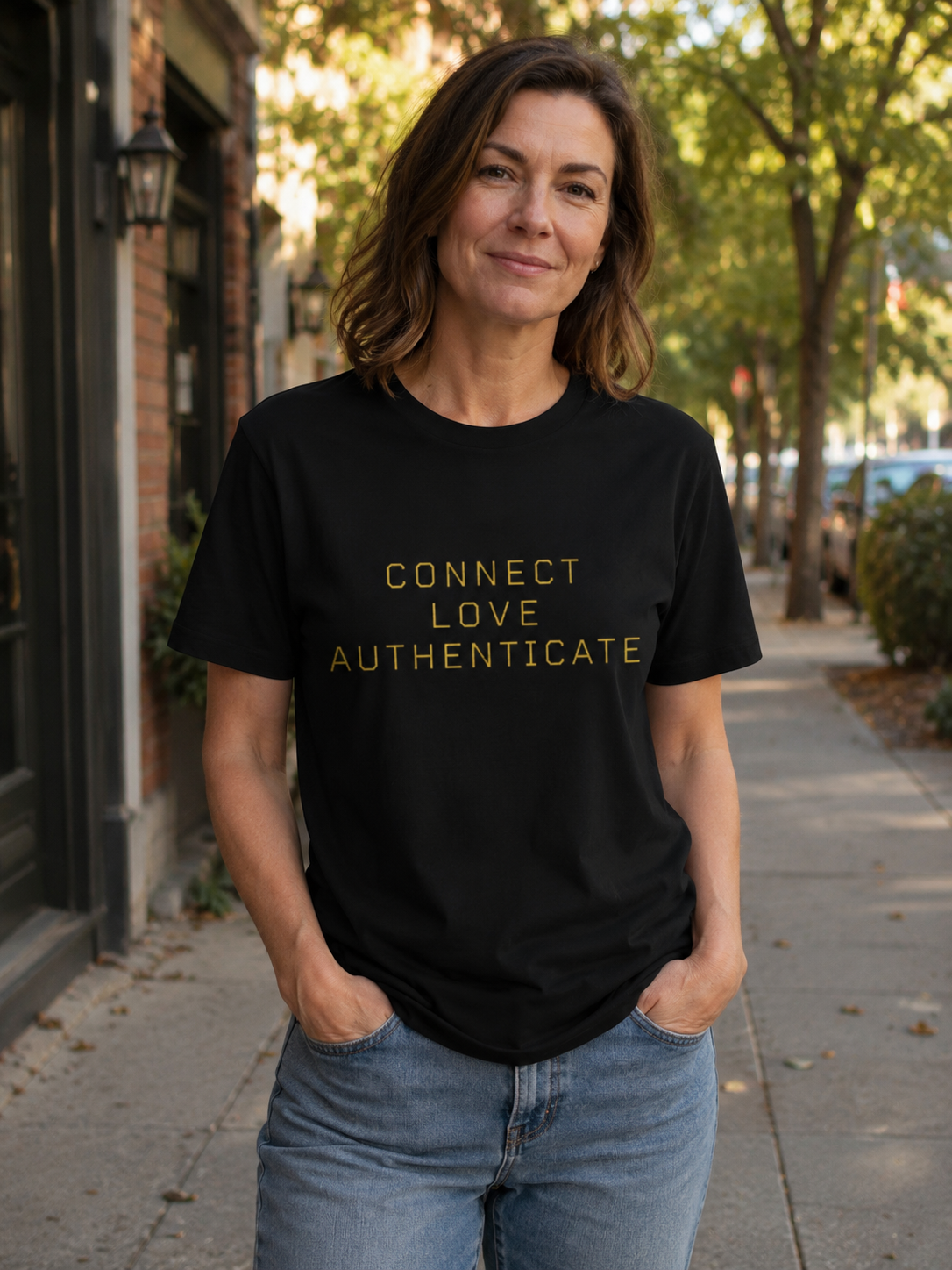 Woman wearing The Human Protocol Tee on a neighborhood sidewalk, featuring gold CONNECT, LOVE, AUTHENTICATE typography on a black T-shirt.