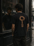 Man wearing The Key Within Tee from behind beside a reflective storefront window, featuring the EVAREN wood-grain key graphic.