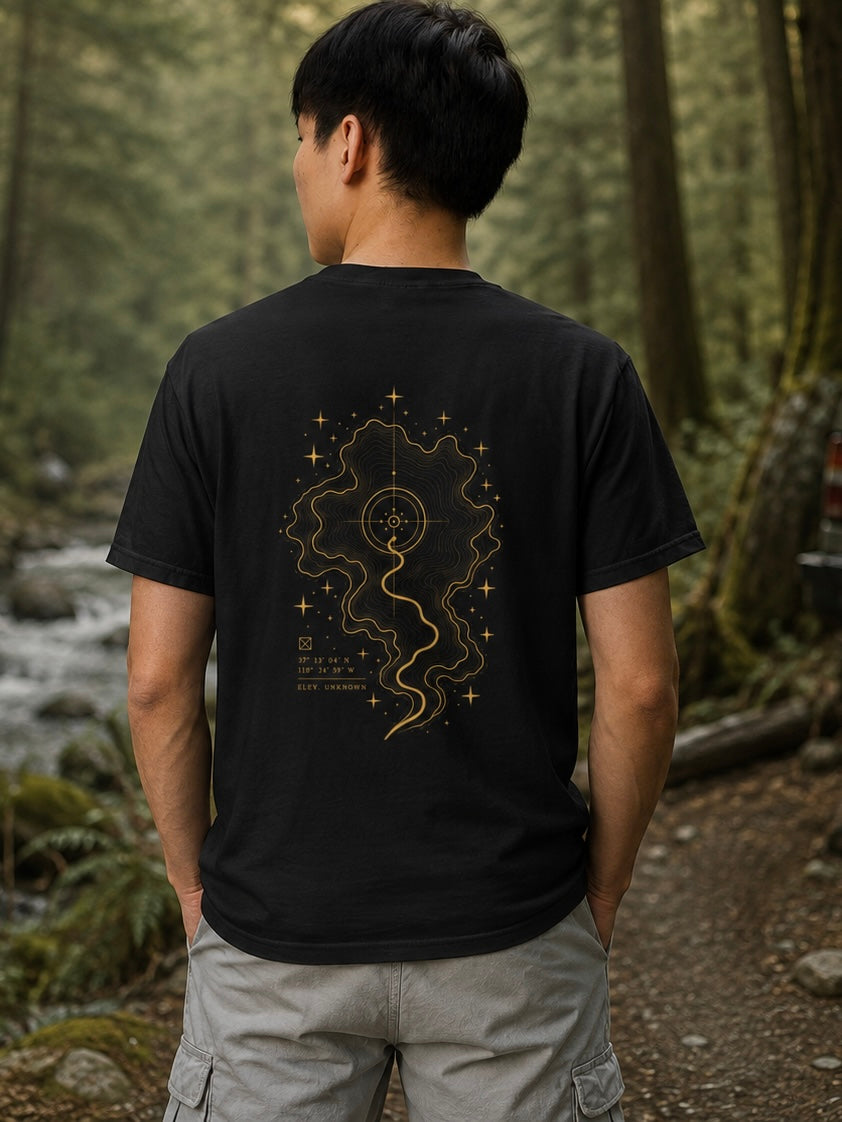 The Inner Map Tee by EVAREN worn in a forest, showing gold topographic path artwork on the back