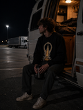 Man wearing The False Ceiling Sweatshirt while sitting in the open doorway of a camper van at a freeway rest stop at night.