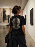 Woman wearing The Parallax Tee in a modern art museum, showing the dual-profile back graphic.