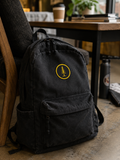 EVAREN Tree Patch on a black canvas backpack in a warm café setting.