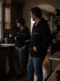 Father and son wearing black EVAREN Side by Side Zip Hoodies together in a lived-in kitchen.