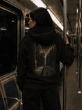 Woman wearing the black EVAREN Headed There Hoodie on a subway, showing the large railway and forest back graphic.