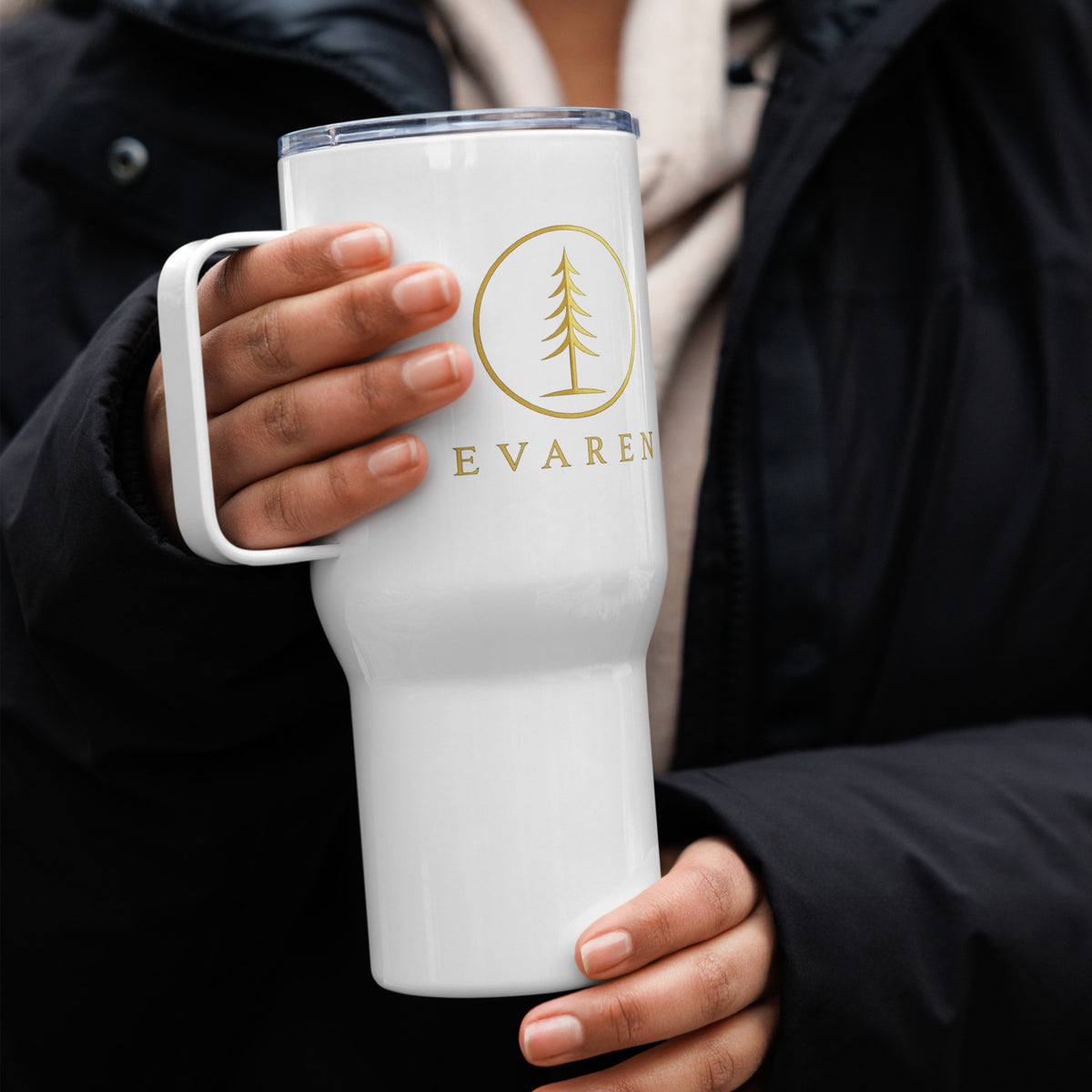 Person holding white EVAREN Travel Tumbler with gold evergreen emblem