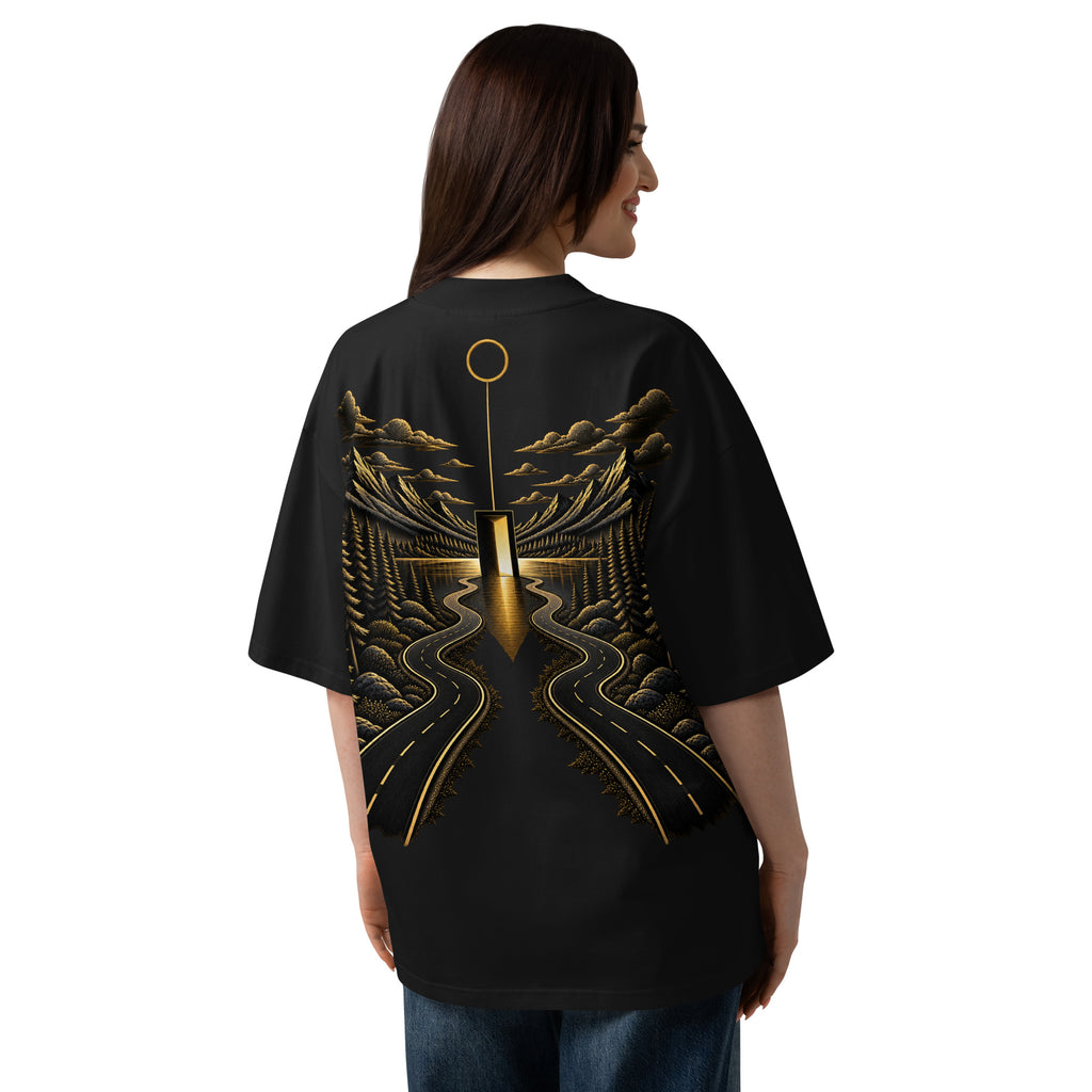 Woman wearing The Roads Tee in black, showing the oversized fit and large gold road and landscape artwork on the back.