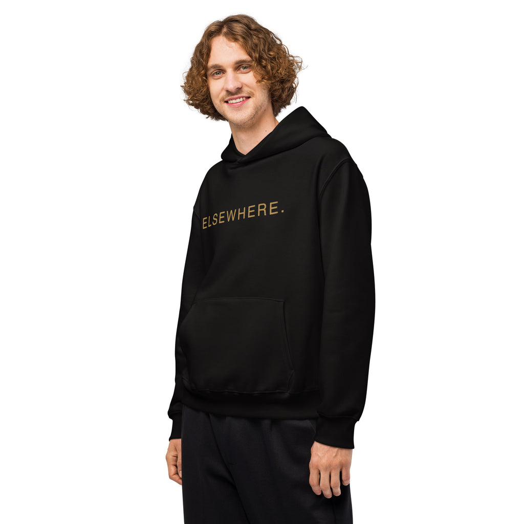 Man wearing the oversized black Elsewhere Hoodie with gold flat embroidery.