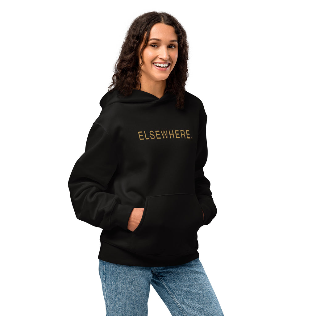 Woman wearing the oversized black Elsewhere Hoodie with gold flat embroidery.