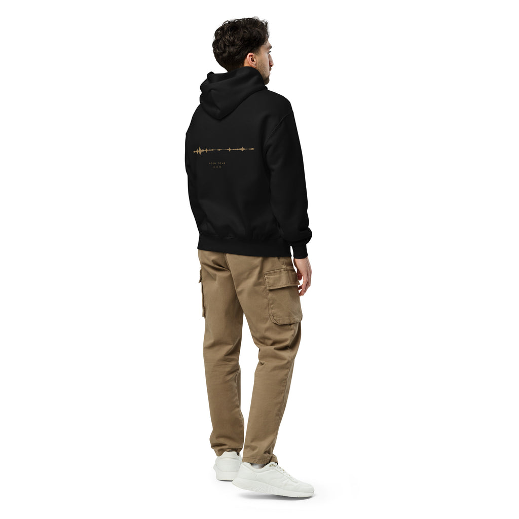 Man wearing the black EVAREN Room Tone Hoodie from an angled back view, showing the relaxed fit and waveform back artwork.