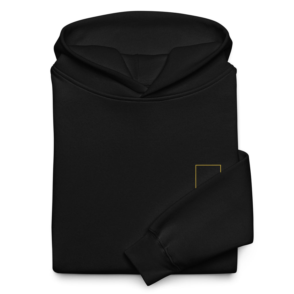Folded black Trap Door Hoodie showing the hood, sleeve, fabric, and small gold chest symbol.